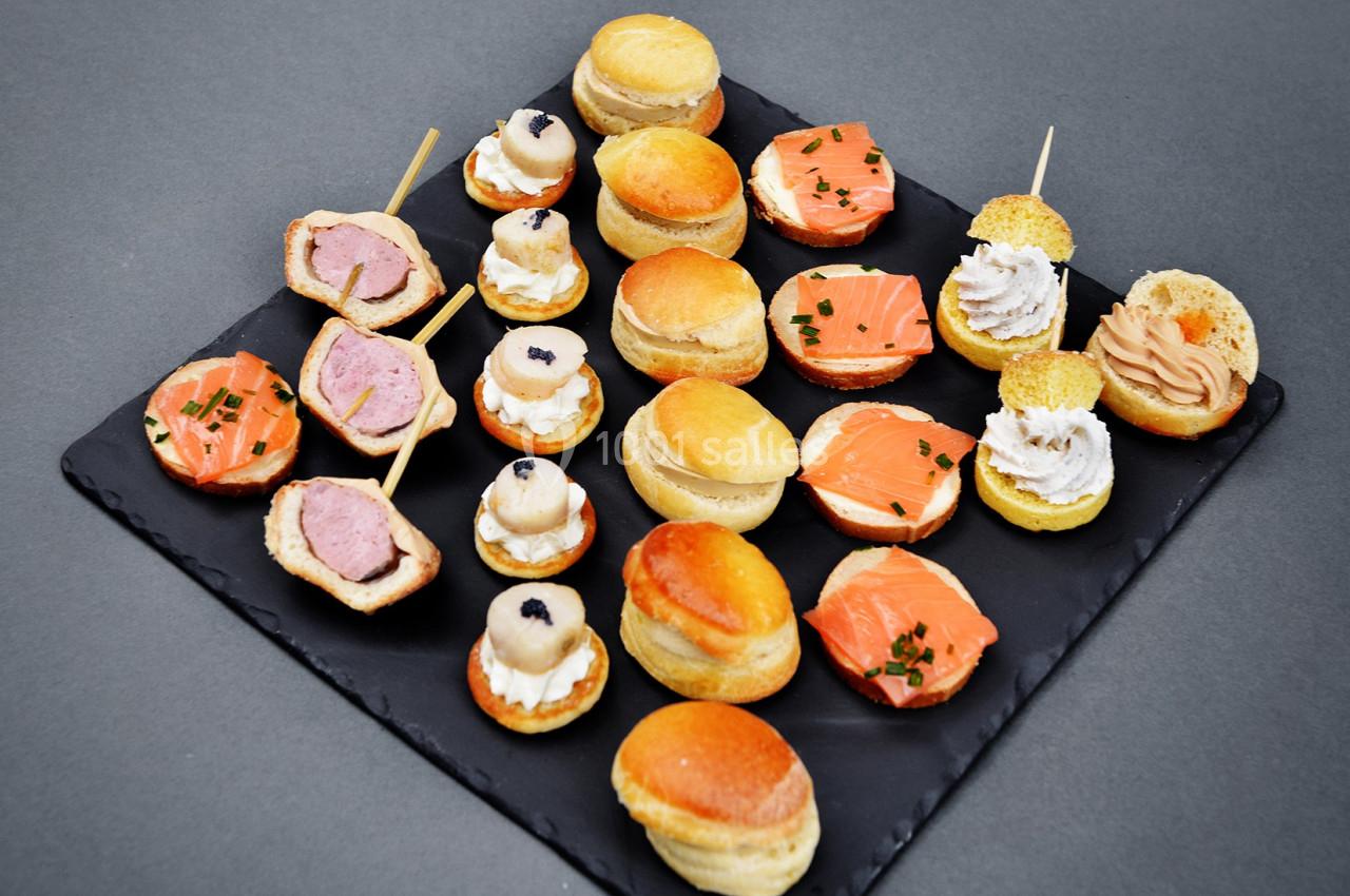 Plateau d'amuse-bouches variés comprenant saumon, foie gras, mousse et mini-bouchées sur ardoise noire.