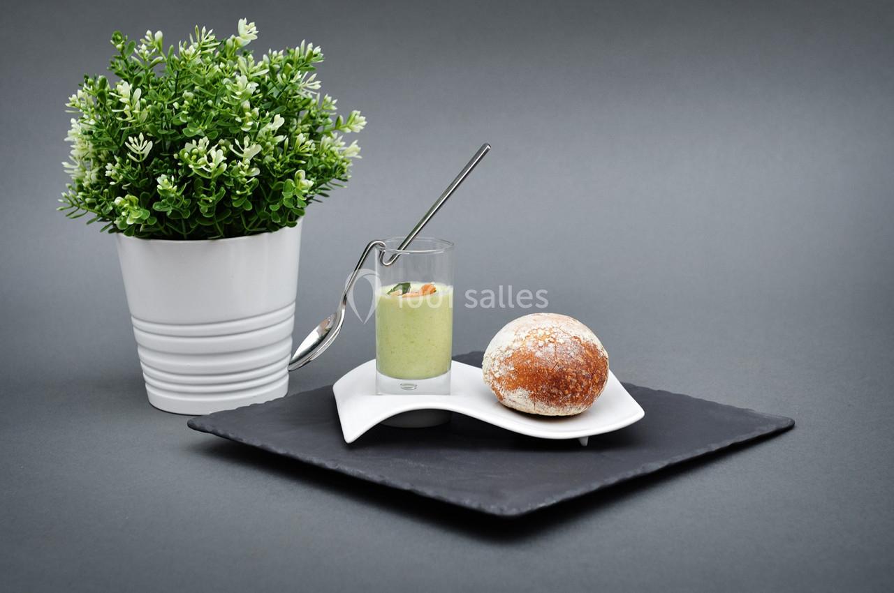 Plante verte en pot à côté d'une verrine de soupe verte avec une cuillère et un petit pain sur une assiette.
