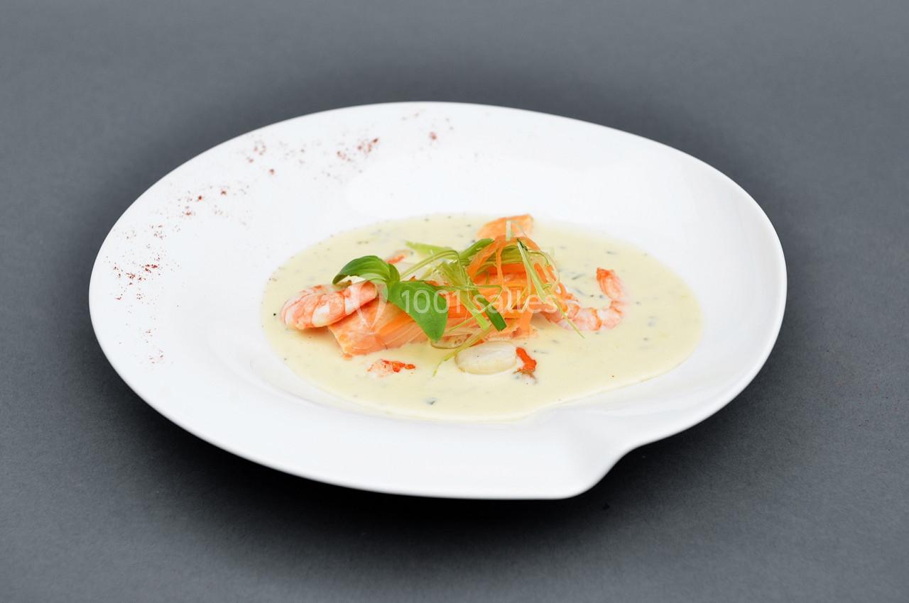 Assiette de crevettes et légumes sur une sauce crémeuse, présentée sur un fond gris.