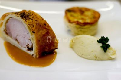 Petit pont en fer forgé traversant un cours d'eau bordé d'arbres, près d'une maison en pierre avec toit en ardoise.