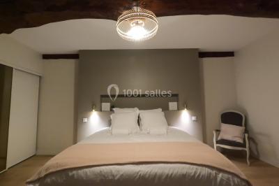 Petit pont en fer forgé traversant un cours d'eau bordé d'arbres, près d'une maison en pierre avec toit en ardoise.