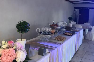 Petit pont en fer forgé traversant un cours d'eau bordé d'arbres, près d'une maison en pierre avec toit en ardoise.