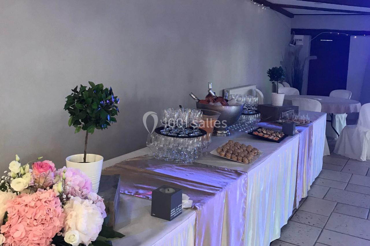 Table de réception dressée avec des fleurs, des verres, des desserts et un seau à champagne dans une salle décorée.