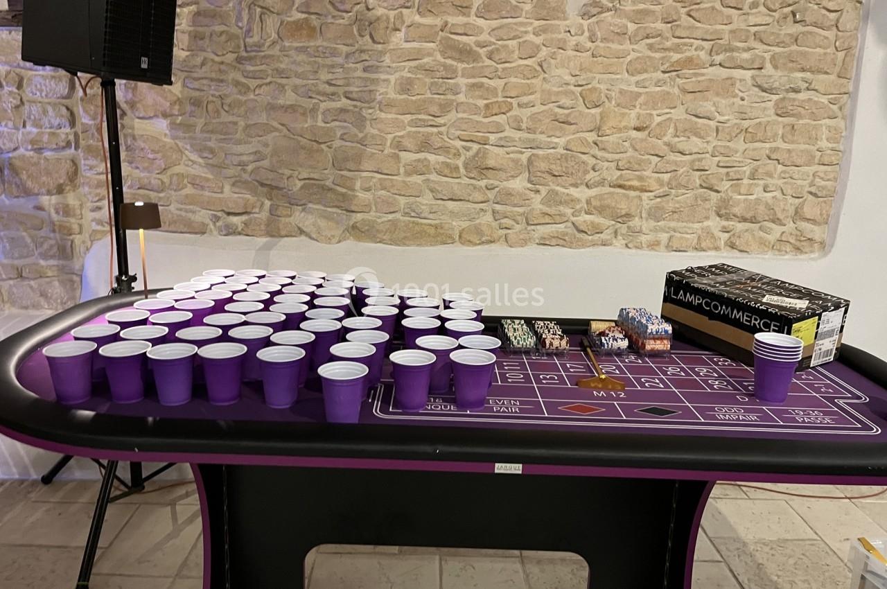 Table de jeu de casino avec des gobelets violets alignés, des jetons et une boîte, devant un mur en pierre.
