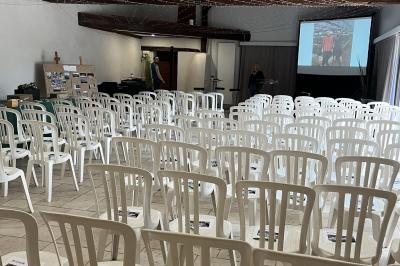 Petit pont en fer forgé traversant un cours d'eau bordé d'arbres, près d'une maison en pierre avec toit en ardoise.