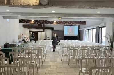 Petit pont en fer forgé traversant un cours d'eau bordé d'arbres, près d'une maison en pierre avec toit en ardoise.