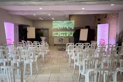 Petit pont en fer forgé traversant un cours d'eau bordé d'arbres, près d'une maison en pierre avec toit en ardoise.