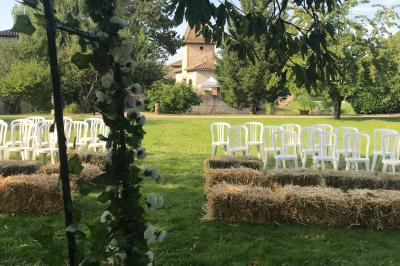 Petit pont en fer forgé traversant un cours d'eau bordé d'arbres, près d'une maison en pierre avec toit en ardoise.