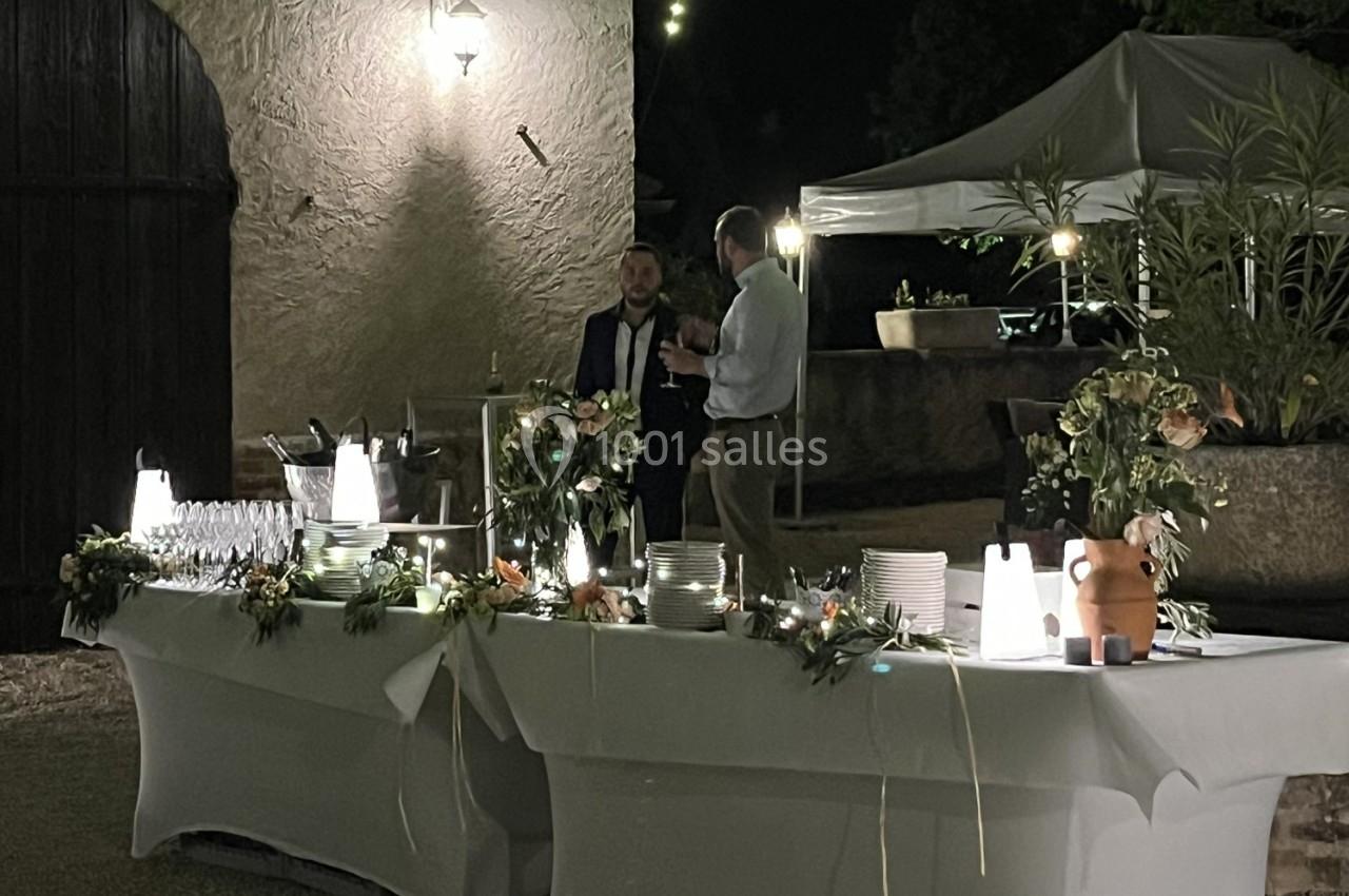 Table de buffet éclairée en extérieur, décorée de fleurs, avec deux hommes discutant à proximité sous un éclairage tamisé.