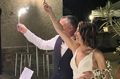 Petit pont en fer forgé traversant un cours d'eau bordé d'arbres, près d'une maison en pierre avec toit en ardoise.