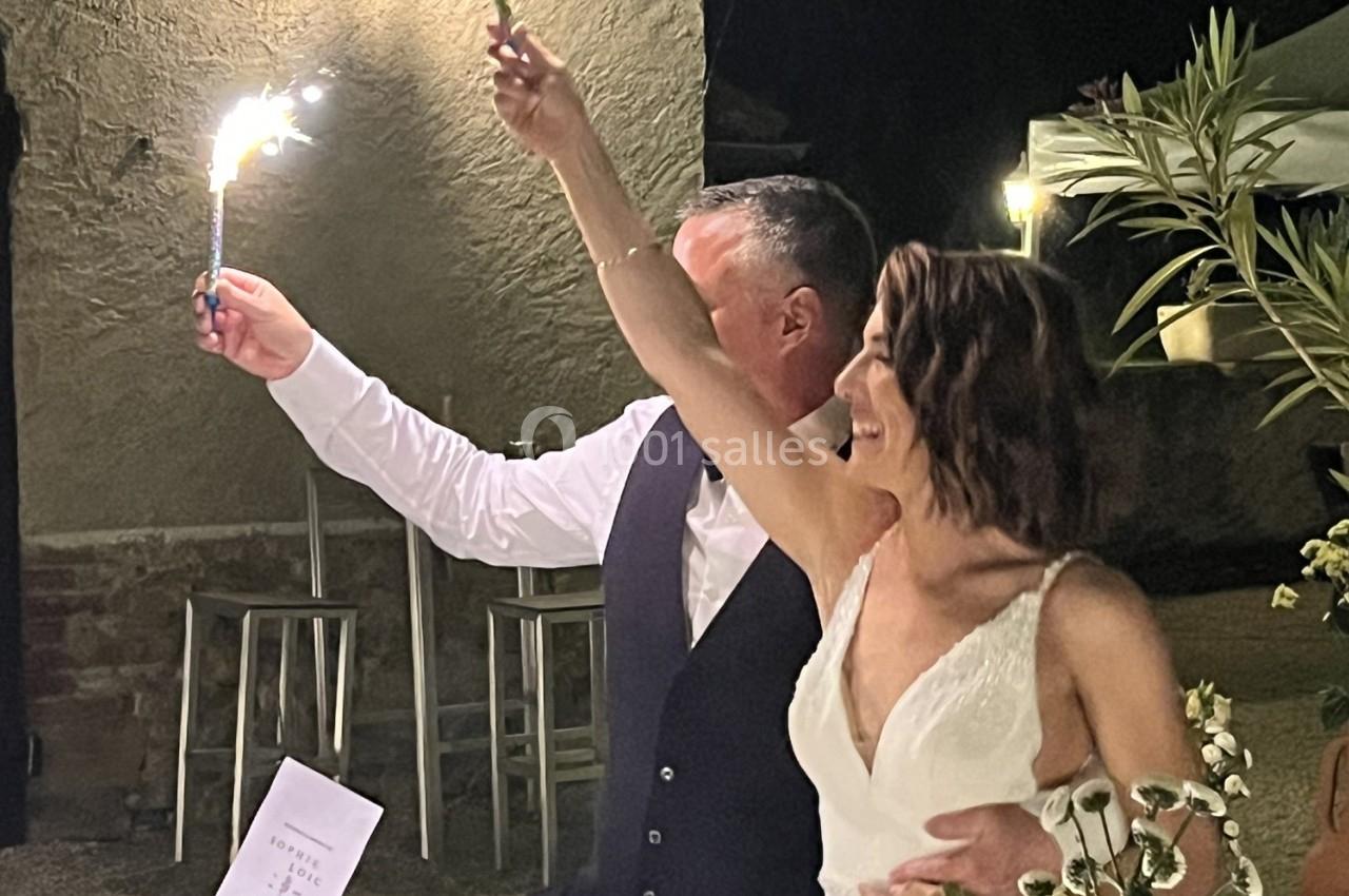 Un couple souriant tenant des cierges magiques allumés lors d'une célébration en soirée à l'extérieur.