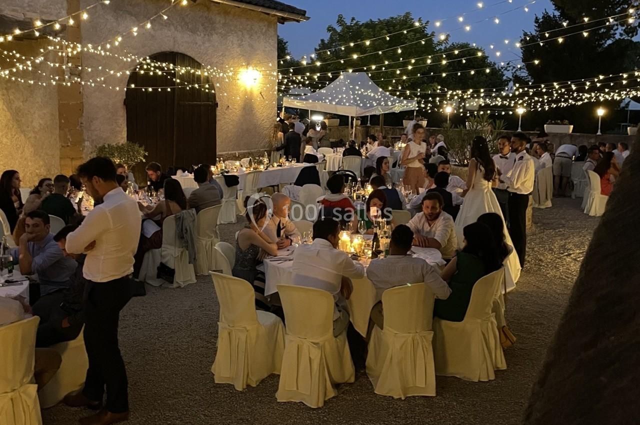 Invités dînant en soirée dans une cour éclairée par des guirlandes lumineuses, ambiance festive et conviviale.