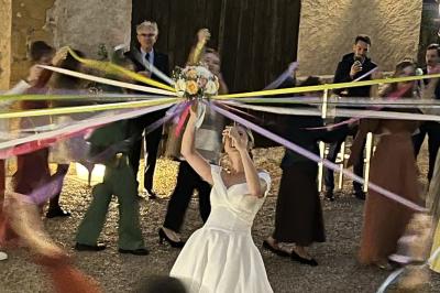 Petit pont en fer forgé traversant un cours d'eau bordé d'arbres, près d'une maison en pierre avec toit en ardoise.