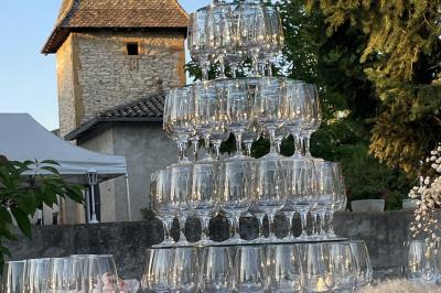 Petit pont en fer forgé traversant un cours d'eau bordé d'arbres, près d'une maison en pierre avec toit en ardoise.