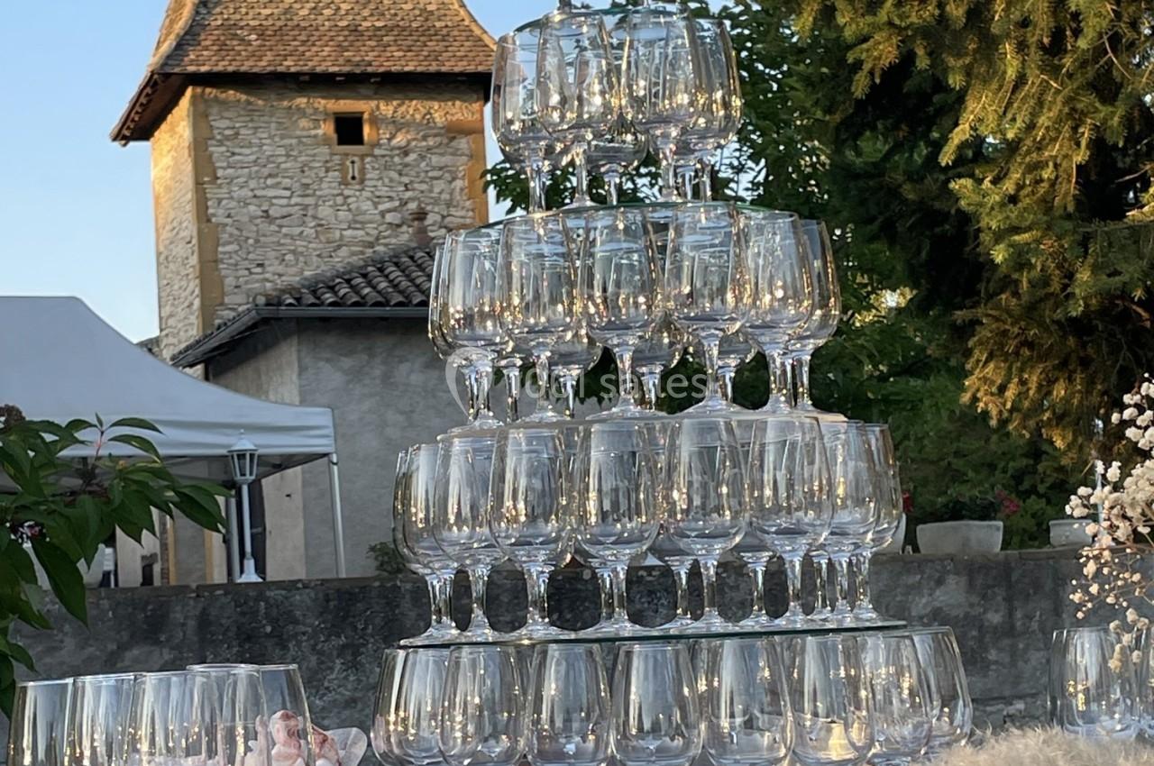 Tour de verres à pied empilés en pyramide, éclairés par la lumière naturelle, avec un bâtiment en pierre en arrière-plan.