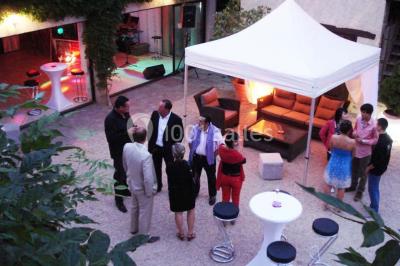 Petit pont en fer forgé traversant un cours d'eau bordé d'arbres, près d'une maison en pierre avec toit en ardoise.