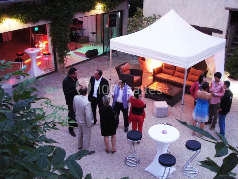 Personnes discutant dans une cour extérieure aménagée avec un barnum, des tables hautes et des fauteuils.