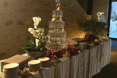 Petit pont en fer forgé traversant un cours d'eau bordé d'arbres, près d'une maison en pierre avec toit en ardoise.