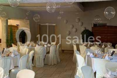 Petit pont en fer forgé traversant un cours d'eau bordé d'arbres, près d'une maison en pierre avec toit en ardoise.