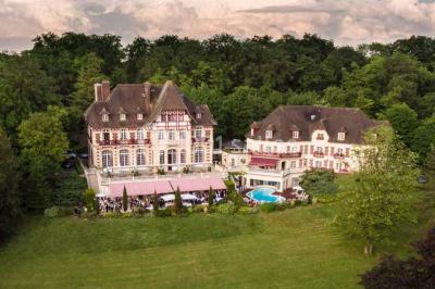 Chambre d'hôtel lumineuse avec lit double, coussins rouges, bureau, télévision et fenêtre donnant sur un balcon fleuri.