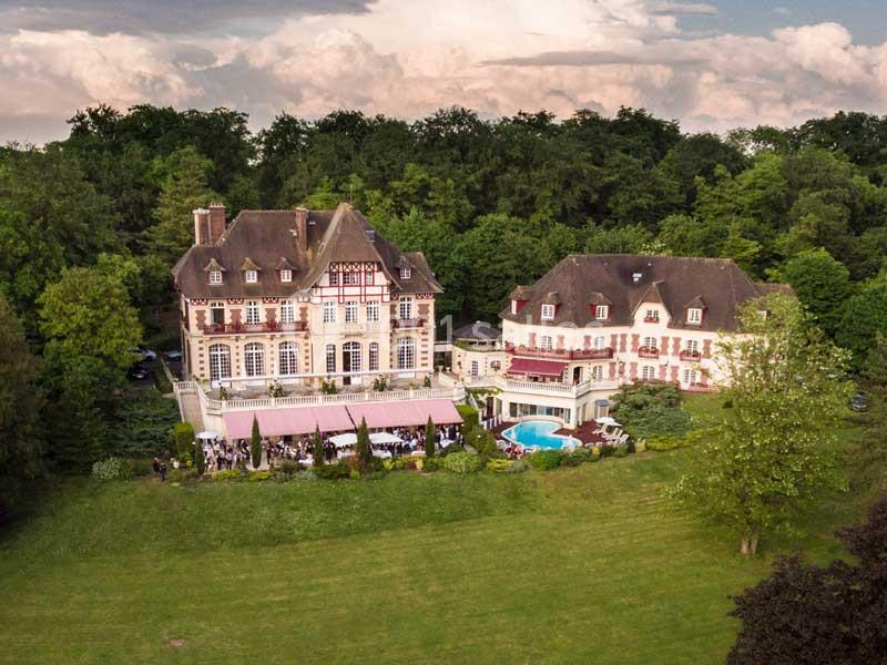Vue aérienne d'un grand domaine avec deux bâtiments élégants, une piscine et un parc arboré environnant.