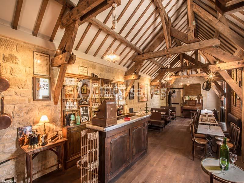 Intérieur d'un bar rustique avec poutres apparentes, comptoir en bois, tables alignées et décoration vintage.