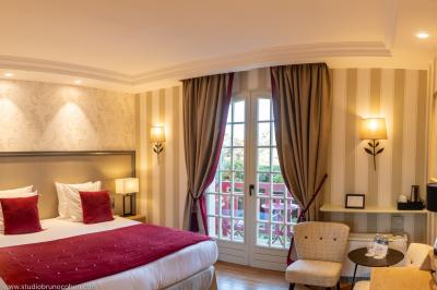 Chambre d'hôtel lumineuse avec lit double, coussins rouges, bureau, télévision et fenêtre donnant sur un balcon fleuri.