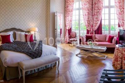 Chambre d'hôtel lumineuse avec lit double, coussins rouges, bureau, télévision et fenêtre donnant sur un balcon fleuri.