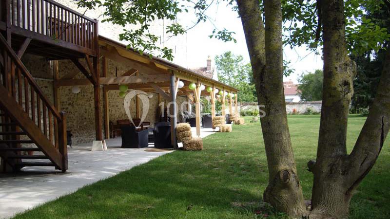 Terrasse couverte en bois avec mobilier extérieur, bordée de pelouse et d'arbres dans un cadre champêtre.