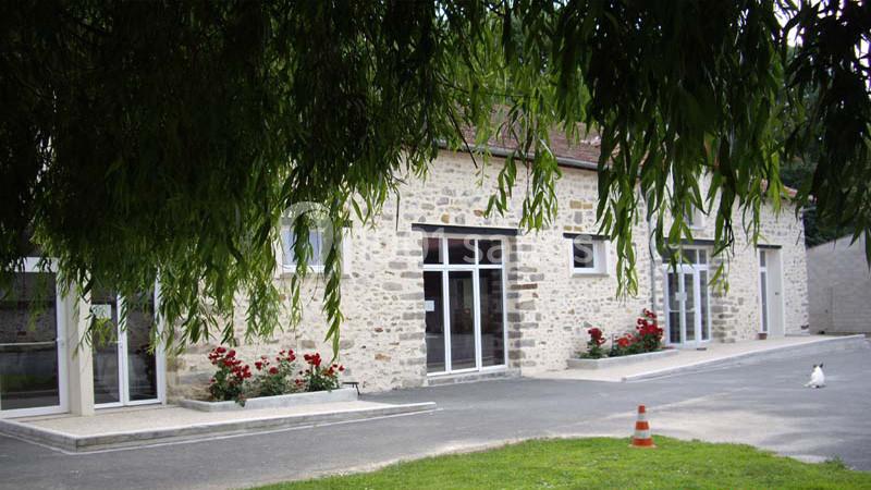 Bâtiment en pierre avec de grandes baies vitrées, entouré de rosiers et d'un espace extérieur pavé et herbeux.