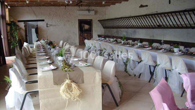 Salle de réception décorée avec deux longues tables alignées, nappes blanches et chaises ornées de housses.