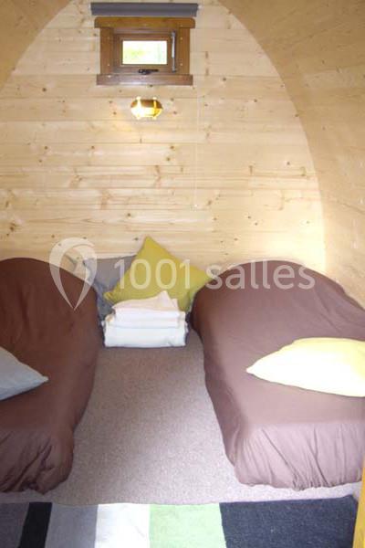 Deux lits simples avec draps bruns, coussins colorés et une petite fenêtre dans une pièce en bois clair.