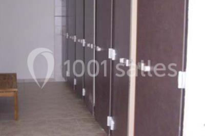 Rangée de cabines de toilettes avec portes en bois foncé, dans un espace carrelé et bien éclairé.