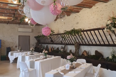 Façade en pierre et brique d'une maison avec rosiers grimpants, jardin verdoyant et terrasse ensoleillée.
