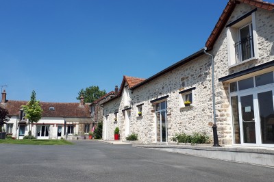Façade en pierre et brique d'une maison avec rosiers grimpants, jardin verdoyant et terrasse ensoleillée.
