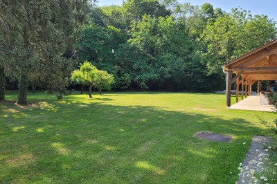 Façade en pierre et brique d'une maison avec rosiers grimpants, jardin verdoyant et terrasse ensoleillée.