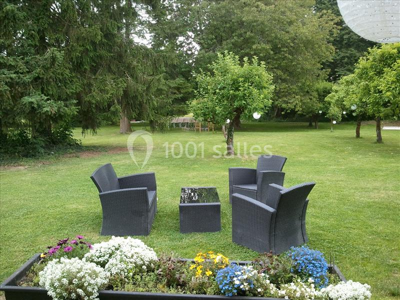 Mobilier de jardin en résine tressée avec table et chaises noires, installé sur une pelouse entourée d'arbres.