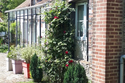 Façade en pierre et brique d'une maison avec rosiers grimpants, jardin verdoyant et terrasse ensoleillée.