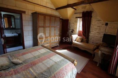 Chambre avec lit double, armoire en bois, canapé et tapis, murs en pierre et plafond avec poutres apparentes.