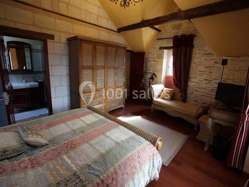 Chambre avec lit double, armoire en bois, fauteuil, bureau, murs en pierre et accès à une salle de bain.