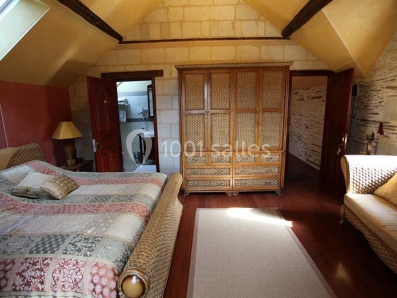 Chambre avec lit double, armoire en bois, canapé et tapis, murs en pierre et plafond avec poutres apparentes.