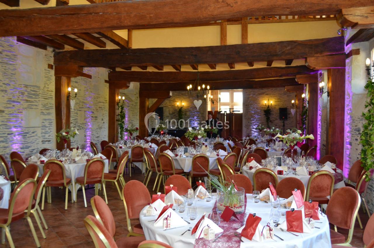 Salle de réception décorée avec des tables rondes dressées, chaises rouges et éclairage tamisé.
