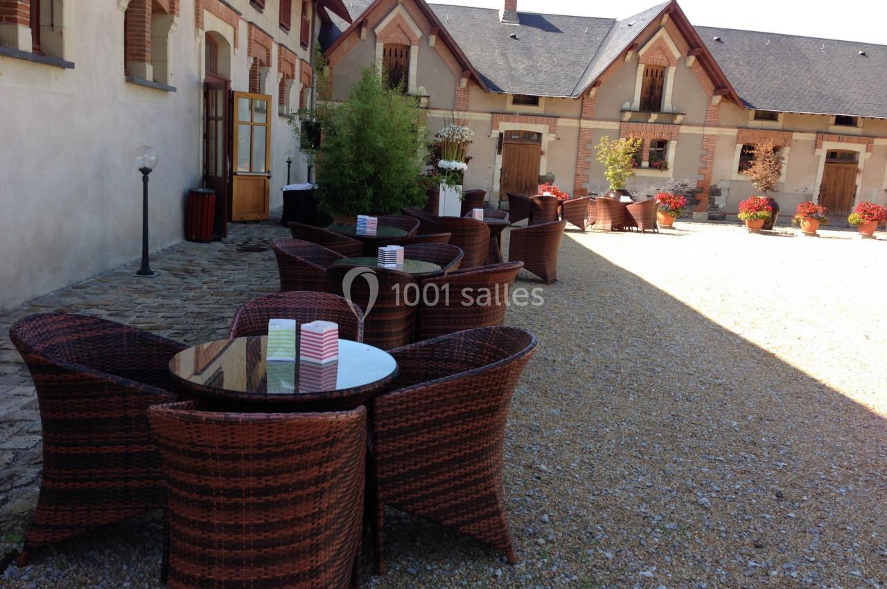 Mobilier en rotin disposé dans une cour pavée devant un bâtiment en briques avec des fenêtres et des fleurs.