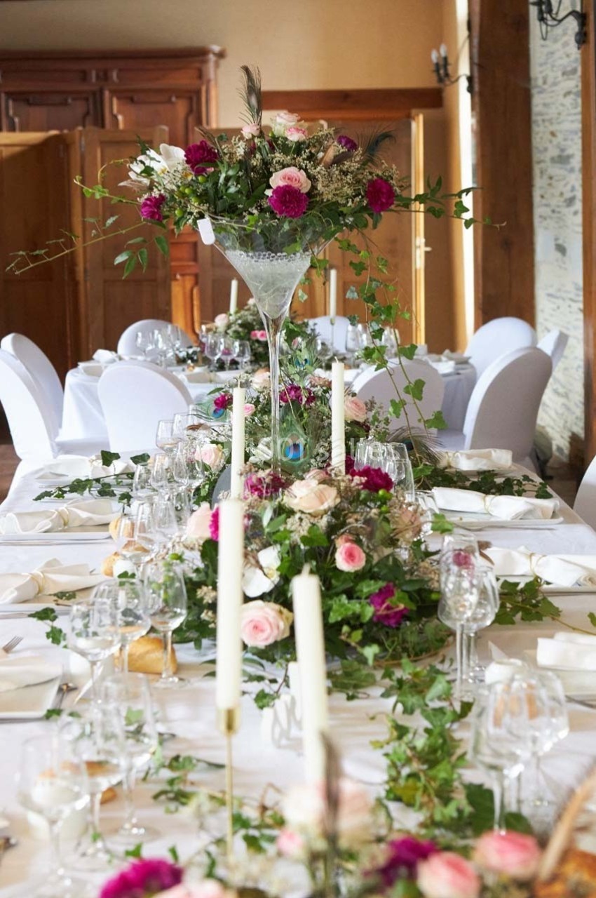 Table de réception décorée avec des fleurs roses et blanches, des chandeliers et des feuillages, dans une salle élégante.