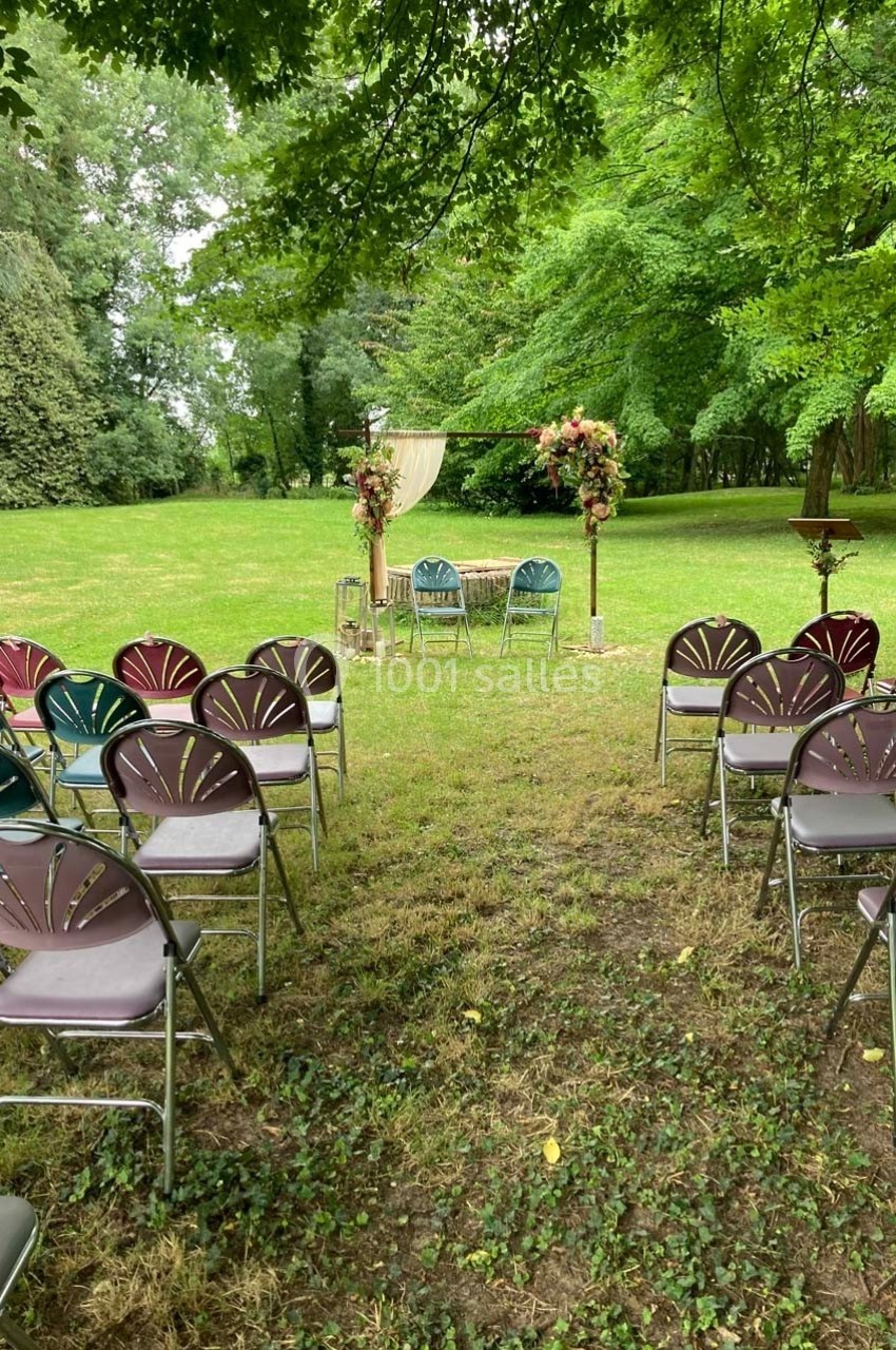 Chaises disposées en rangées face à une arche décorée de fleurs dans un jardin verdoyant pour une cérémonie en plein air.