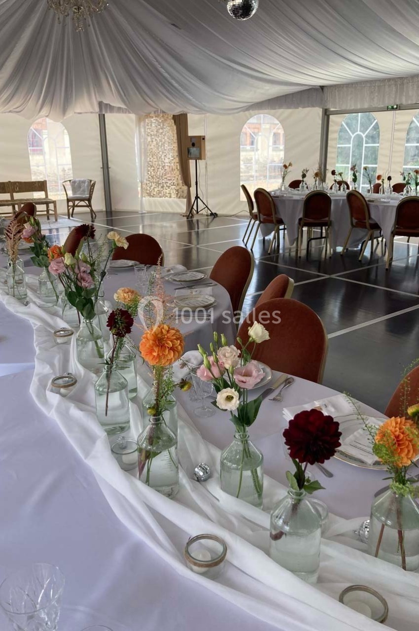 Salle de réception décorée avec des tables blanches ornées de fleurs colorées dans des vases en verre.