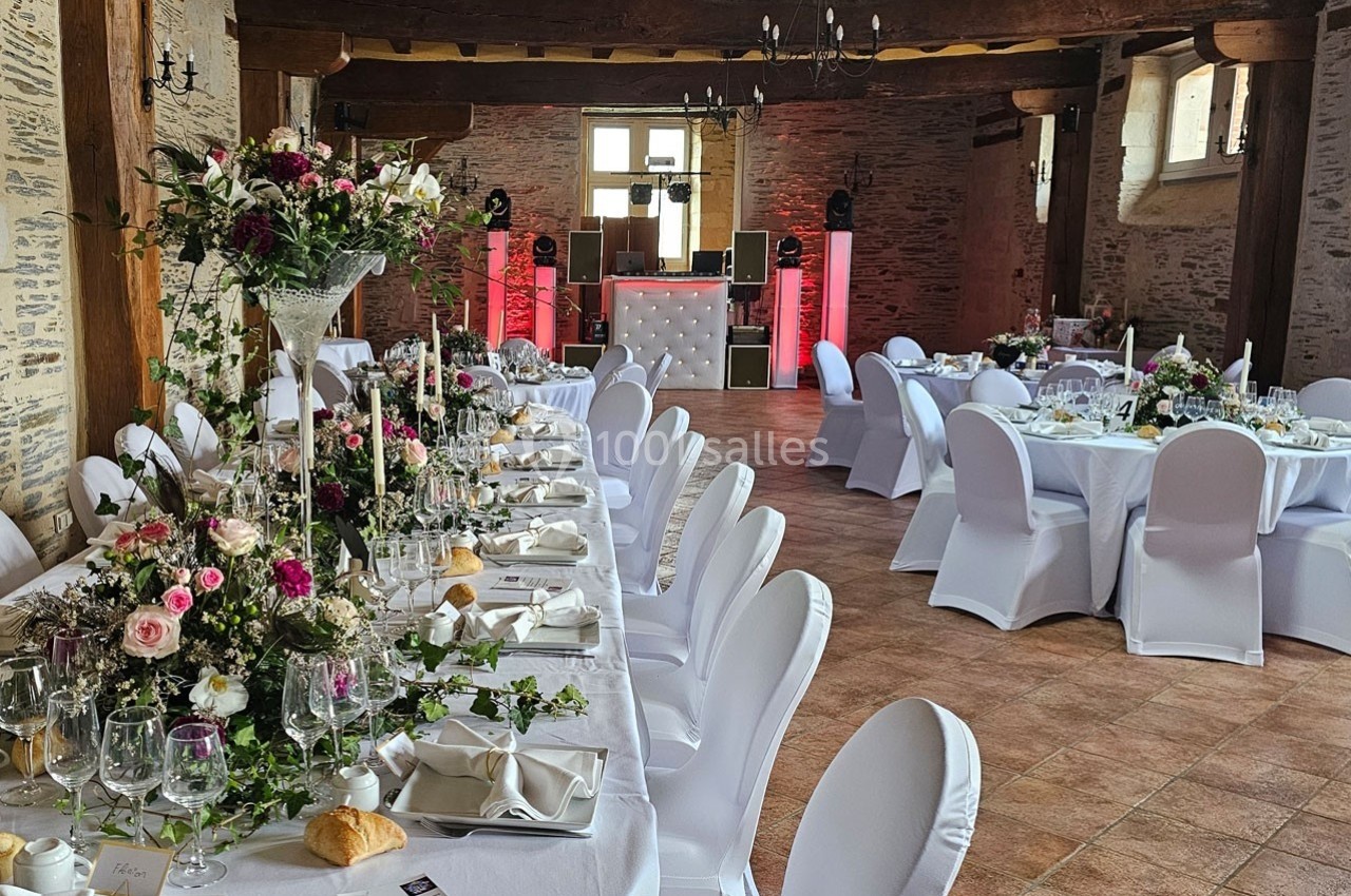 Salle de réception décorée avec des tables dressées, des chaises blanches et des arrangements floraux élégants.