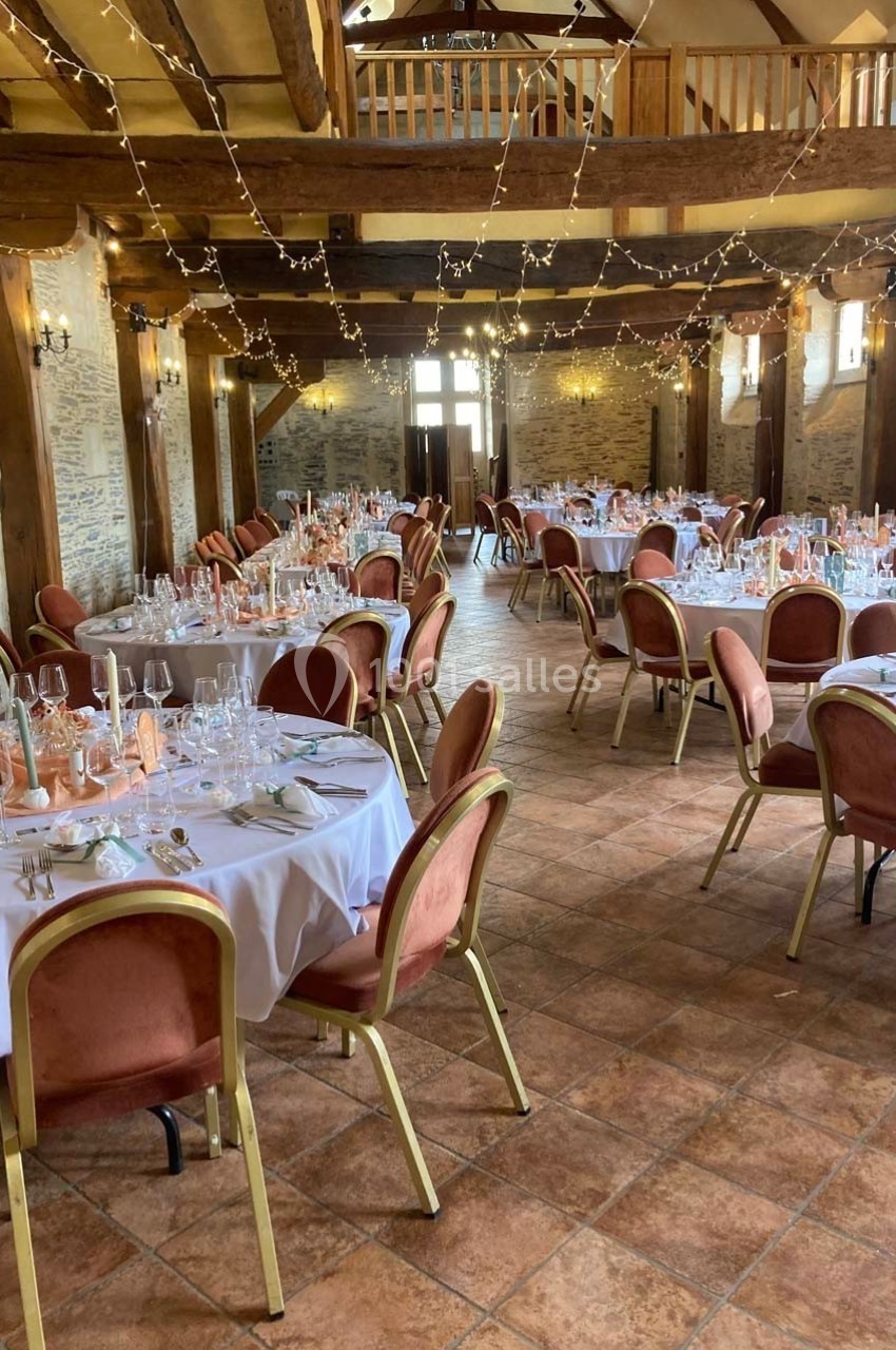 Salle de réception décorée avec des tables rondes dressées, chaises rouges et guirlandes lumineuses suspendues.