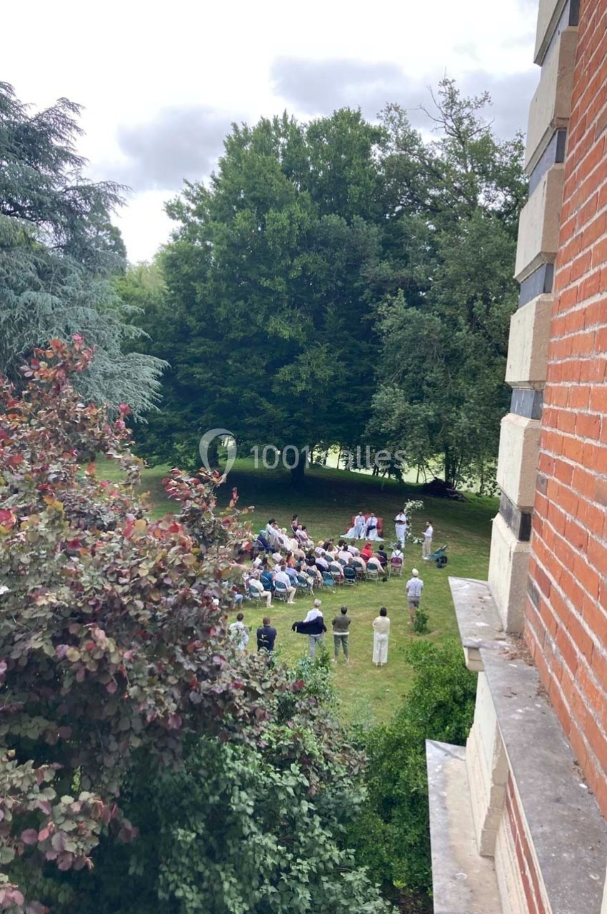 Groupe de personnes assises en cercle dans un jardin verdoyant, vu depuis une fenêtre d'un bâtiment en briques.