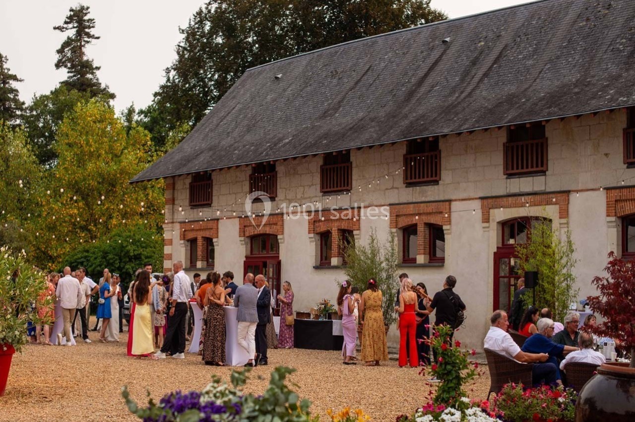 Groupe de personnes rassemblées dans une cour devant un bâtiment en pierre, décoré de guirlandes lumineuses.